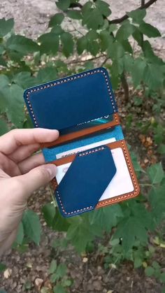 a hand holding an empty wallet in front of some leaves and bushes with one card slot open