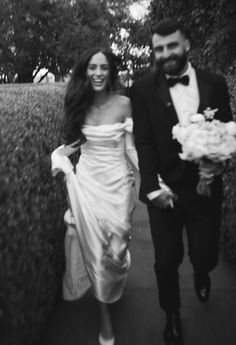 a bride and groom are walking down the sidewalk together in black and white, holding hands