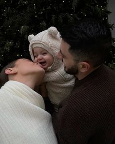 a man and woman kissing a baby in front of a christmas tree