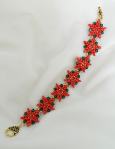 a red and green beaded bracelet on a white surface with gold clasps,