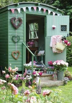 a small green shed with flowers in the front yard and decorations on the outside wall