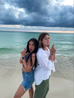 two girls standing on the beach with their arms in the air