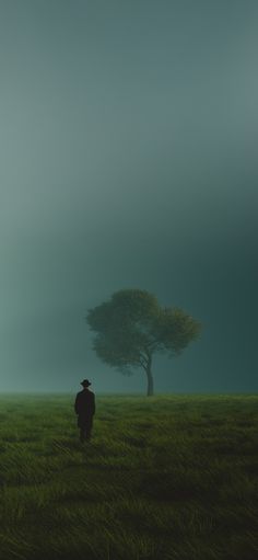 a man standing in the middle of a field with a tree behind him on a foggy day