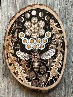 a wooden plaque with a bee and flowers on it's side, sitting on a piece of wood