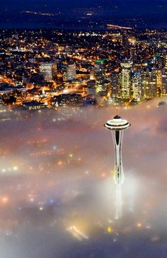 an aerial view of the space needle and city lights in the foggy night sky