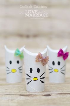 three white cups with cat faces painted on them, one has a pink bow and the other has a green bow