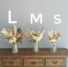 three vases filled with dried flowers sitting on top of a wooden table