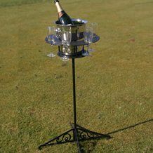 a bottle of wine is sitting on top of a stand in the grass with two glasses