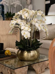 a glass table topped with a vase filled with white flowers next to a couch and chair