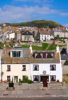 a white house sitting on the side of a road in front of a hill covered with houses