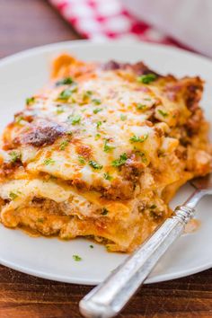 a white plate topped with lasagna covered in cheese and sauce next to a fork