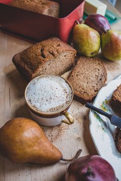 bread, pears and other fruit on a table with a cup of coffee in the foreground