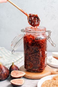 a jar filled with jam sitting on top of a table next to sliced figs