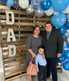 a man, woman and child standing in front of a backdrop with blue and white balloons