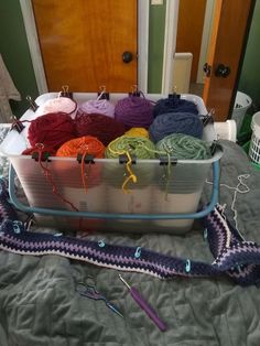 there are many yarns and crochet hooks in the container on the bed