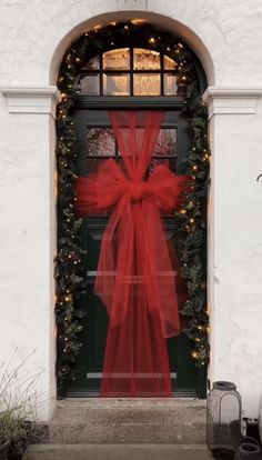 a red bow on the front door of a white house with christmas lights around it