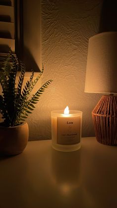 a lit candle sitting on top of a table next to a potted plant