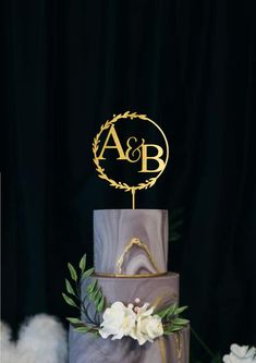 a three tiered wedding cake with gold monogrammed initials and flowers on top