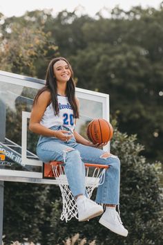 a young woman sitting on top of a basketball hoop holding a basketball in her hand