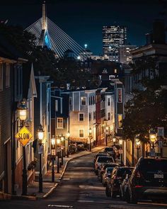 a city street at night with cars parked on both sides and buildings in the background