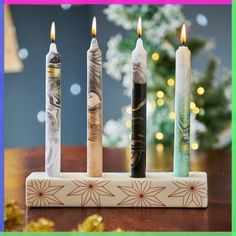 four candles are lined up in a row on a table with a christmas tree in the background