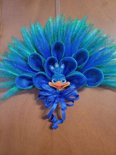 a blue and green peacock head with feathers on it's face, sitting on top of a wooden table