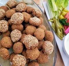 a glass bowl filled with meatballs next to a plate of salad and lettuce