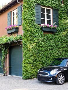 a black car parked in front of a house covered in green plants and ivys