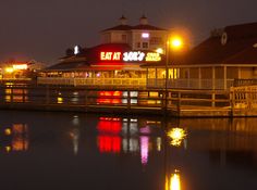 the lights shine brightly on the water and buildings in the background at night, along with a boardwalk that leads to an eatery