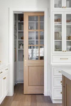 a kitchen with white cabinets and wood flooring next to a wooden door that has glass inserts on it