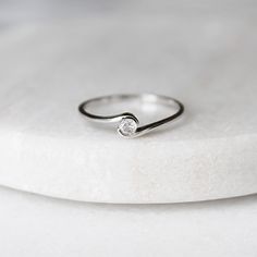 a diamond ring sitting on top of a white marble slab with a small round diamond in the middle