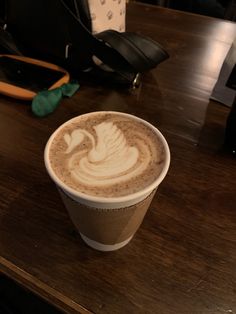 a cappuccino is sitting on a wooden table next to a black bag