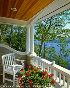 a porch with two white chairs and a potted plant on the front deck overlooking water