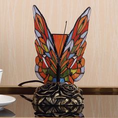 a stained glass butterfly lamp sitting on top of a table next to a cup and saucer