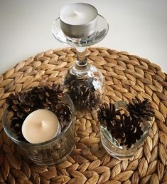 pine cones are placed in glass bowls on a woven place mat next to a candle