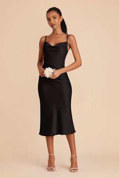 a woman wearing a black dress with spaghetti straps and flowers in her hair, posing for the