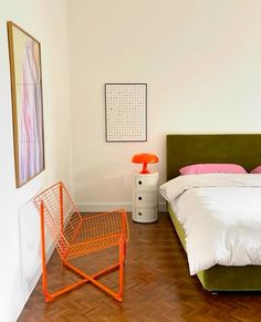 a bed room with a neatly made bed and an orange chair next to the bed