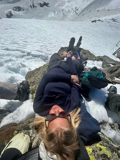 two people laying on the ground in front of some snow covered mountains and glaciers