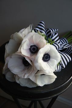 an arrangement of white and black flowers sitting on top of a table next to a wall