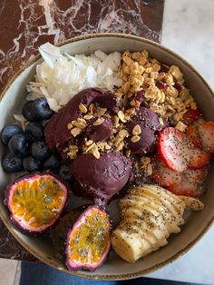 a bowl filled with fruit and nuts on top of a marble table next to a person