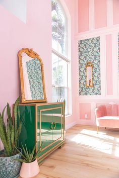 a living room with pink walls, green cabinet and gold mirror on the wall above it