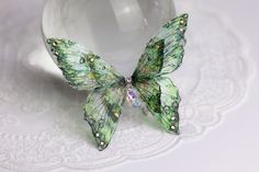 a green butterfly figurine sitting on top of a white doily next to a glass ball