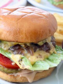 a cheeseburger with lettuce, tomato and onion on a plate next to french fries