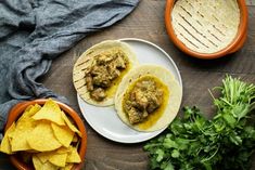 two tacos on a plate with tortillas and cilantro next to it