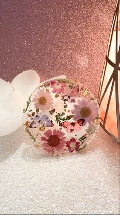 a white vase with pink and purple flowers on it next to a small glass container