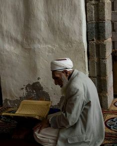 an old man sitting on the floor in front of a wall with a book open