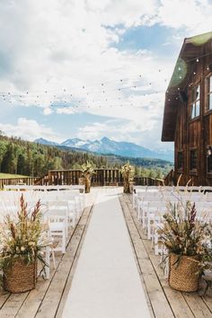 an outdoor ceremony setup with white chairs and flower baskets on the aisle, in front of a rustic building