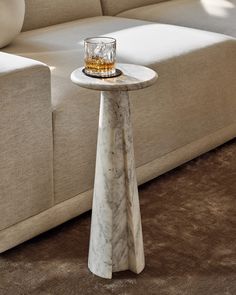 a marble side table with a glass on it in front of a beige sectional couch