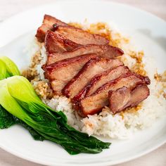 a white plate topped with meat and rice next to green leafy veggies