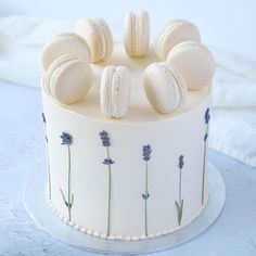 a white cake with macaroons and lavender flowers on the top is sitting on a blue tablecloth